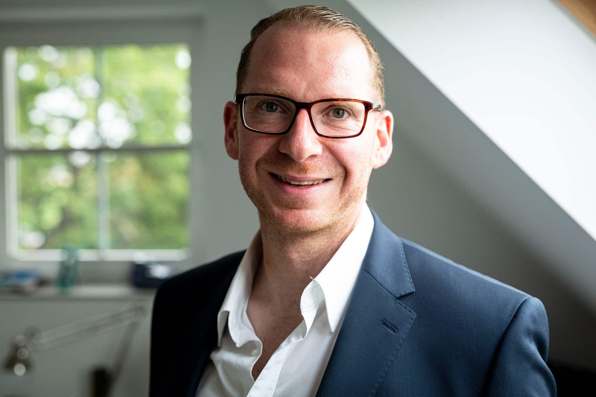 omGa_e1Q Andreas Burdack, Inhaber der Immobilien, steht vor einem Fenster in einem modernen Büro.